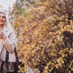 Готовимся к холодам: женщина блондинка в белом пальто с кофе в руках возле дерева с желтыми листьями